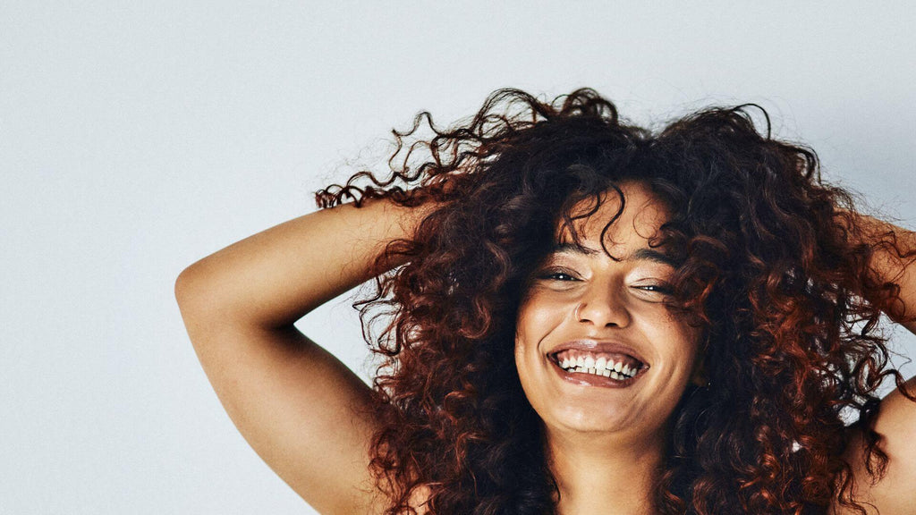 woman with curly hair hands in hair smiling